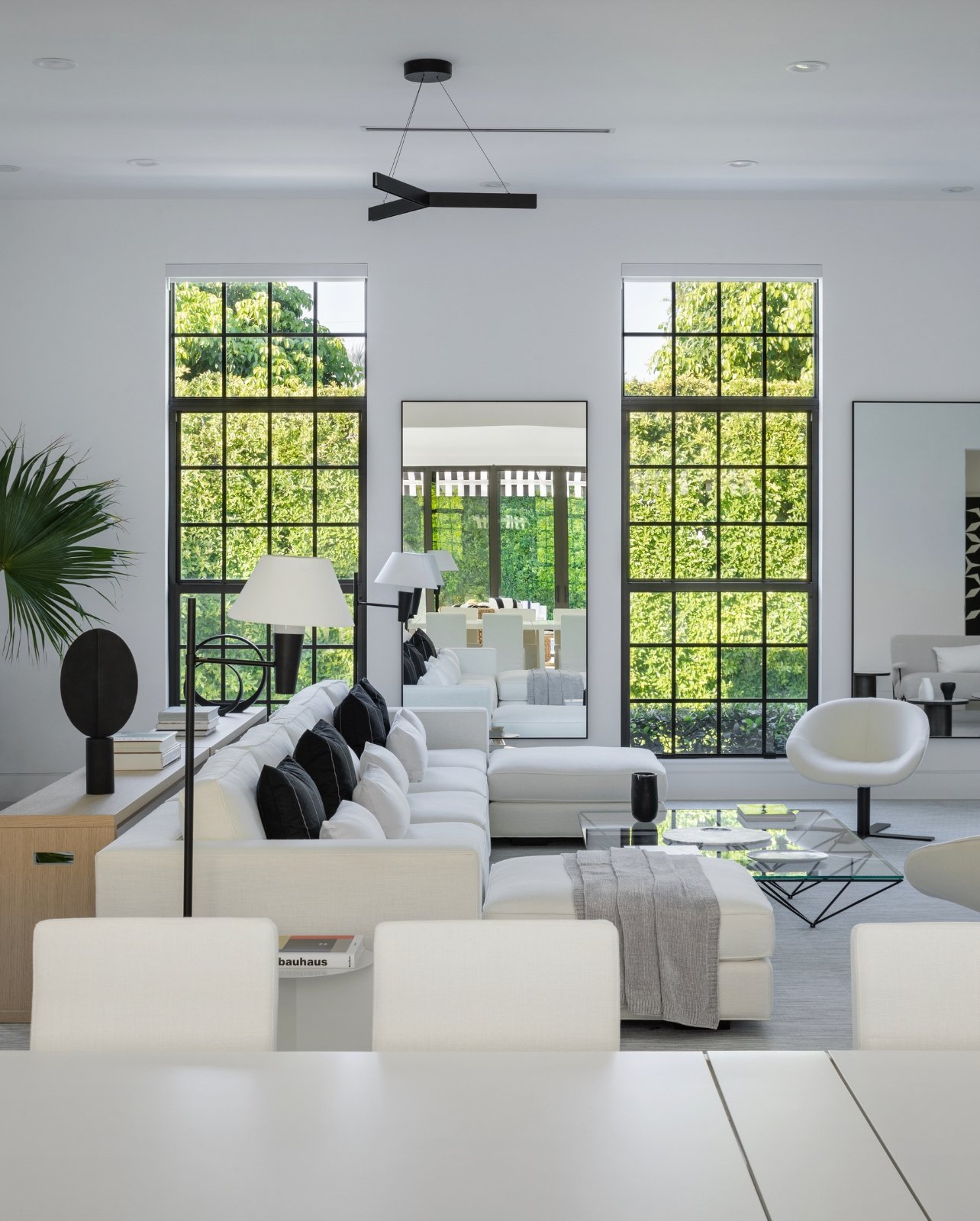 A bright living room with white furniture, black accents, sculptural décor and tall windows