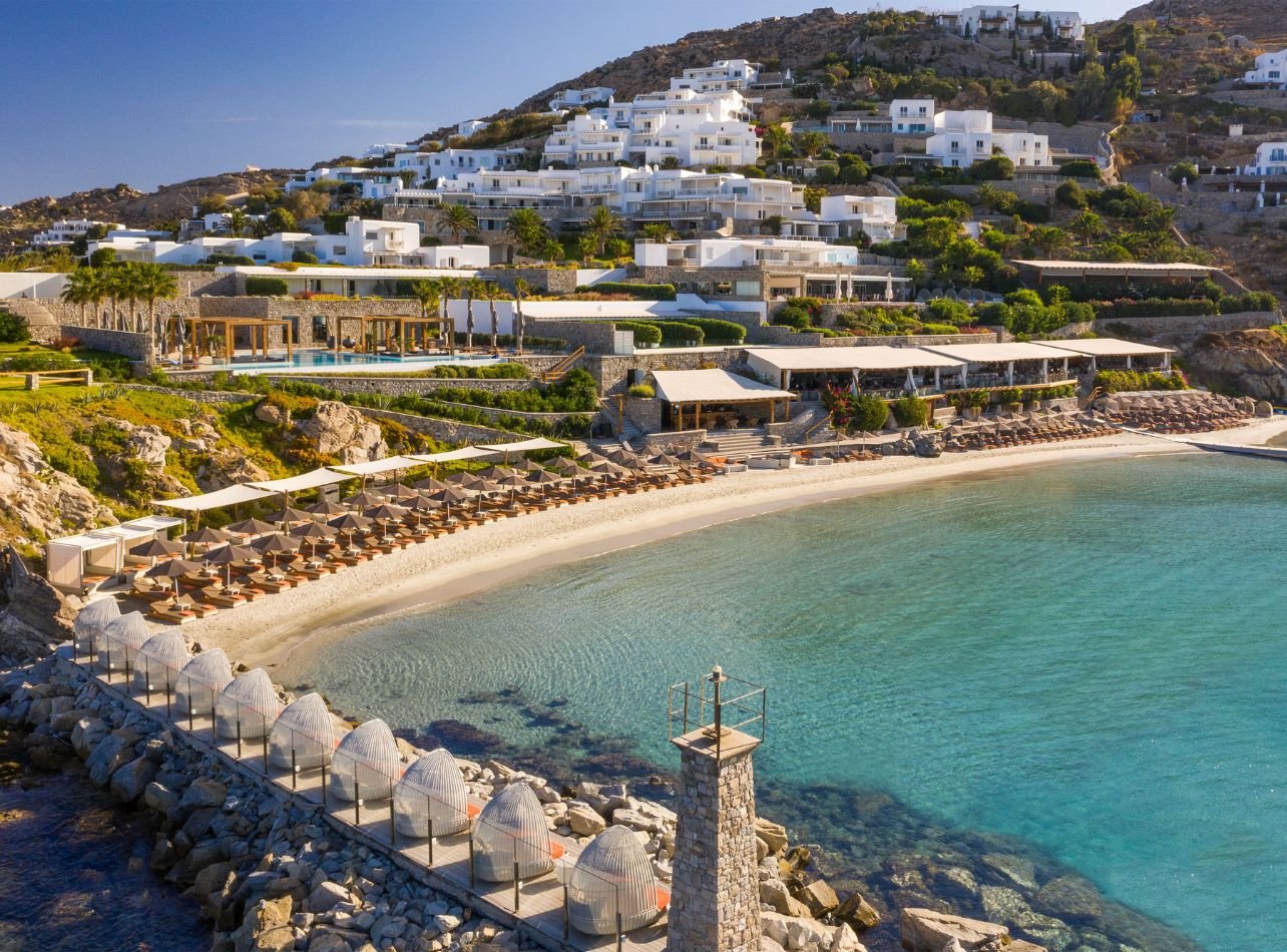 Exterior view of an outdoor bar and restaurant with wooden furnishings and decor at Santa Marina resort in Ornos Bay, Mykonos