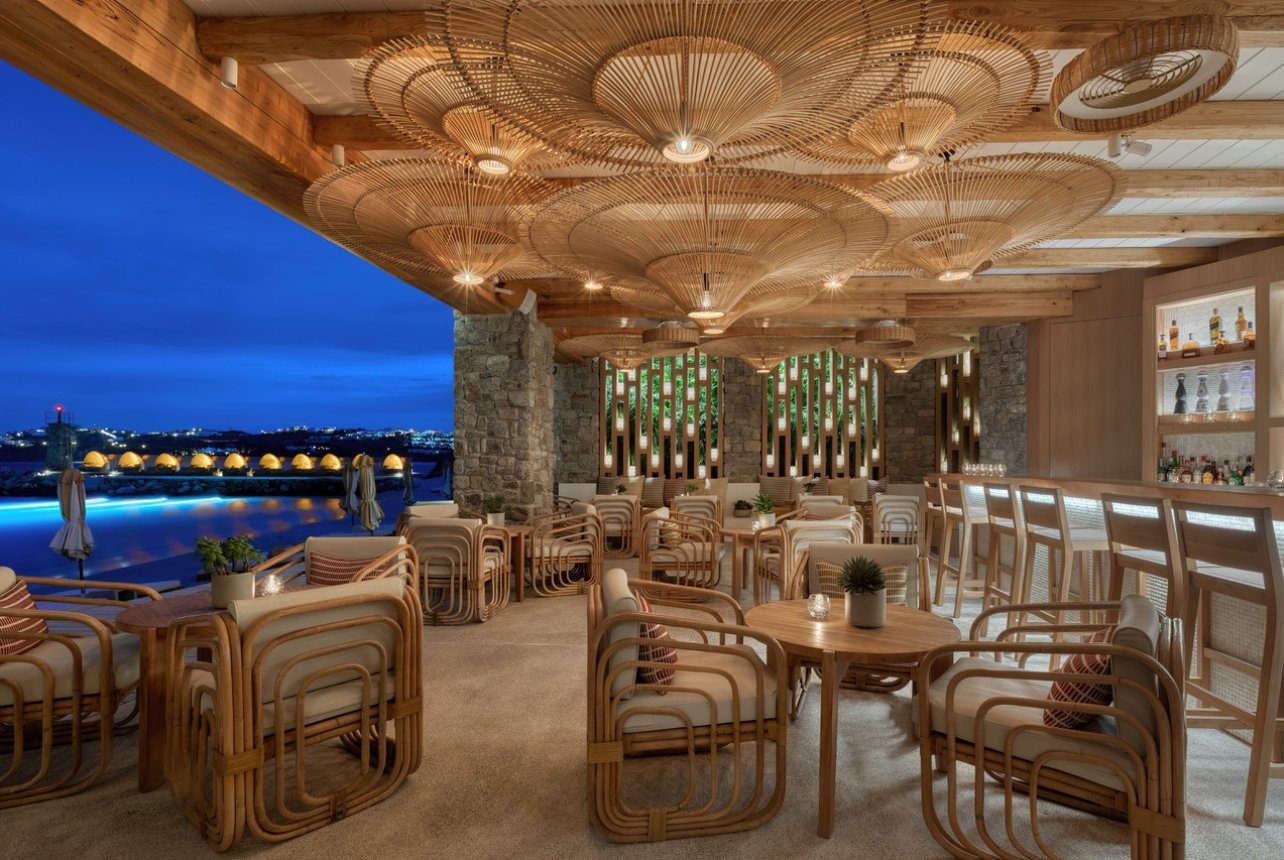Exterior view of an outdoor bar and restaurant with wooden furnishings and decor at Santa Marina resort in Ornos Bay, Mykonos