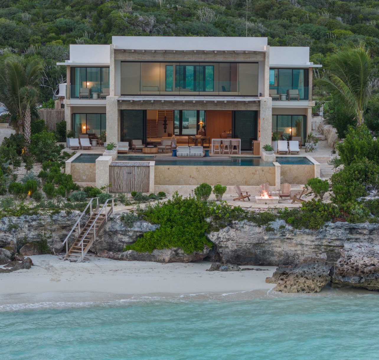 An exterior view of the 82 room complex with an infinity pool and firepit at The Strand on Cooper Jack Bay