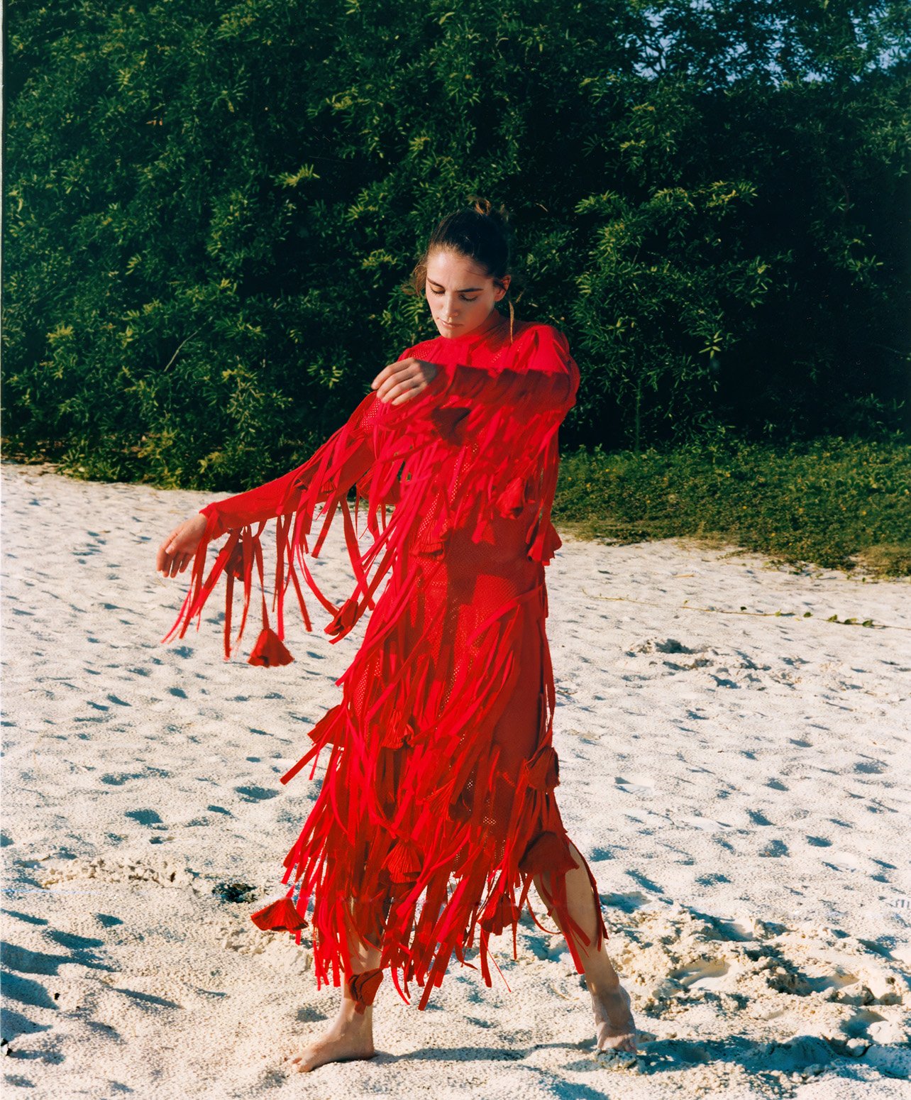 Fashion model standing on a sandy beach with a long red fringe dress