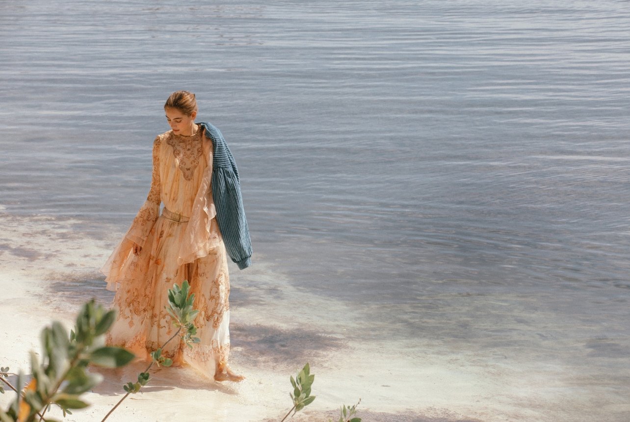 Fashion model standing in the ocean with a flowy maxi dress and blue jacket
