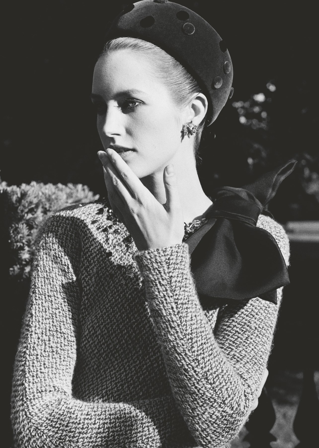 Black and white photo of a fashion model in a polka dot hat, diamond earrings, and a large shoulder bow