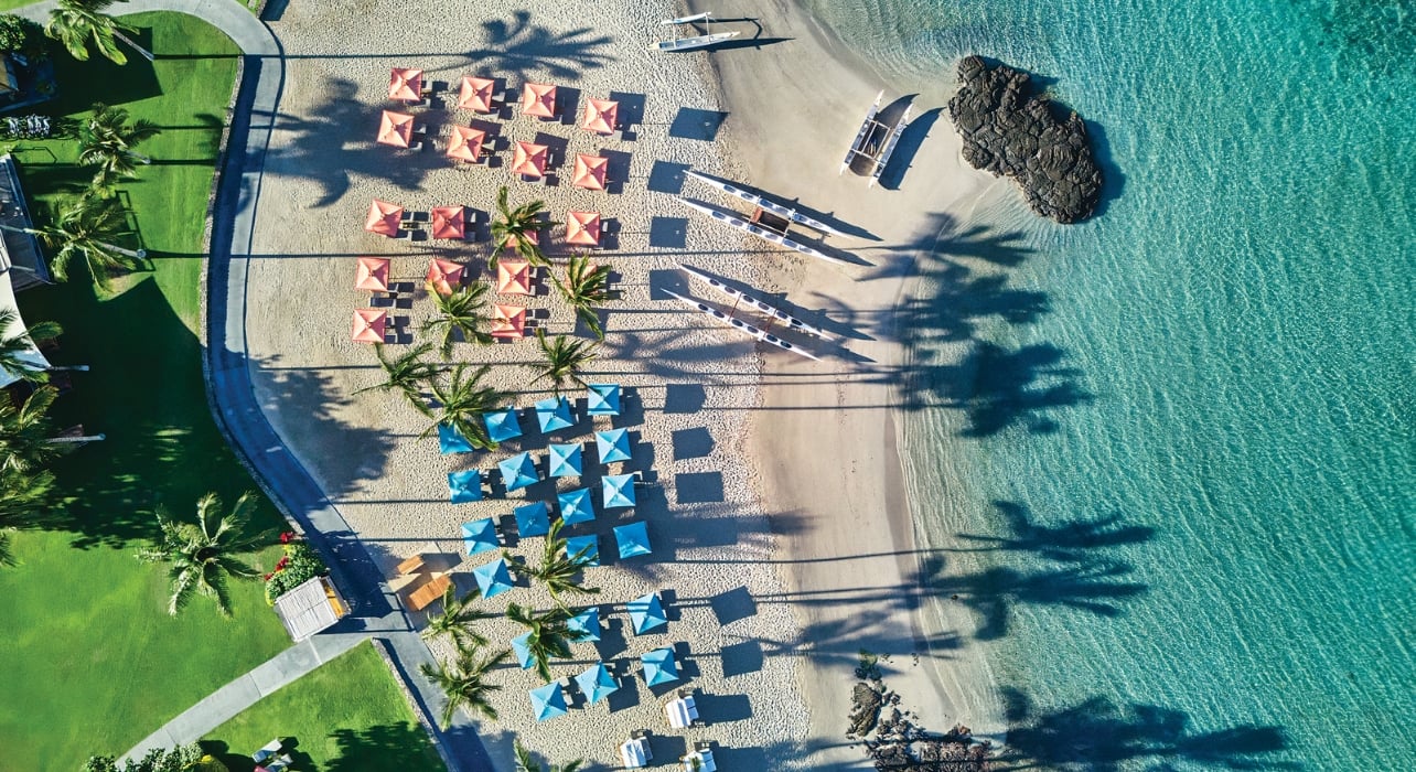 Aerial shot of The Beach Club at Mauna Lani with crystal blue water, boats, and beach umbrellas