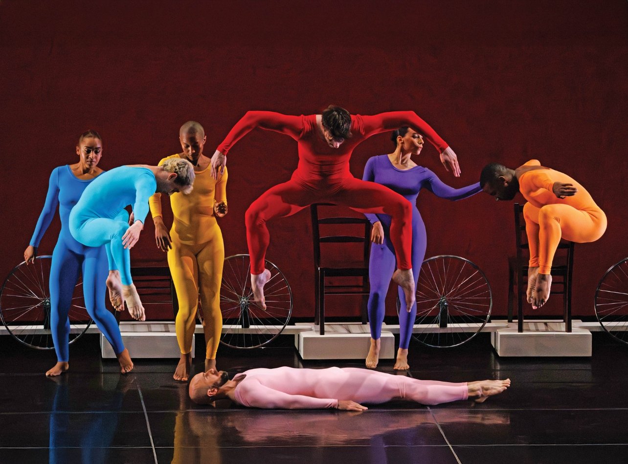 A photo of seven people dressed in colorful bodysuits doing a dance performance on stage for opening night of Travelogue (1979)
