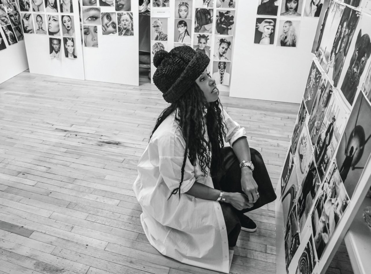 A black and white candid photo of June Ambrose looking at fashion model printouts