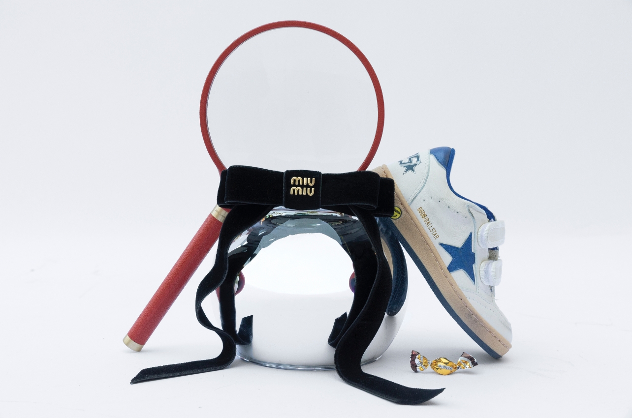 A still life photo of a magnifying glass, a black velvet hair clip, and star sneakers
