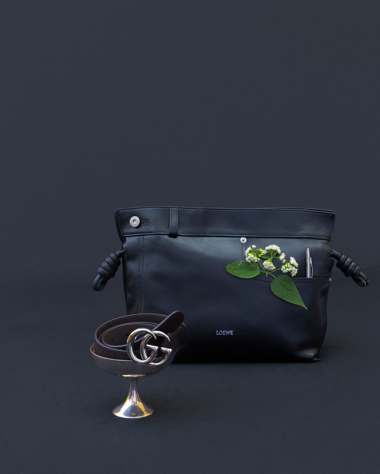 A still-life photograph of a purse and a belt with a flower
