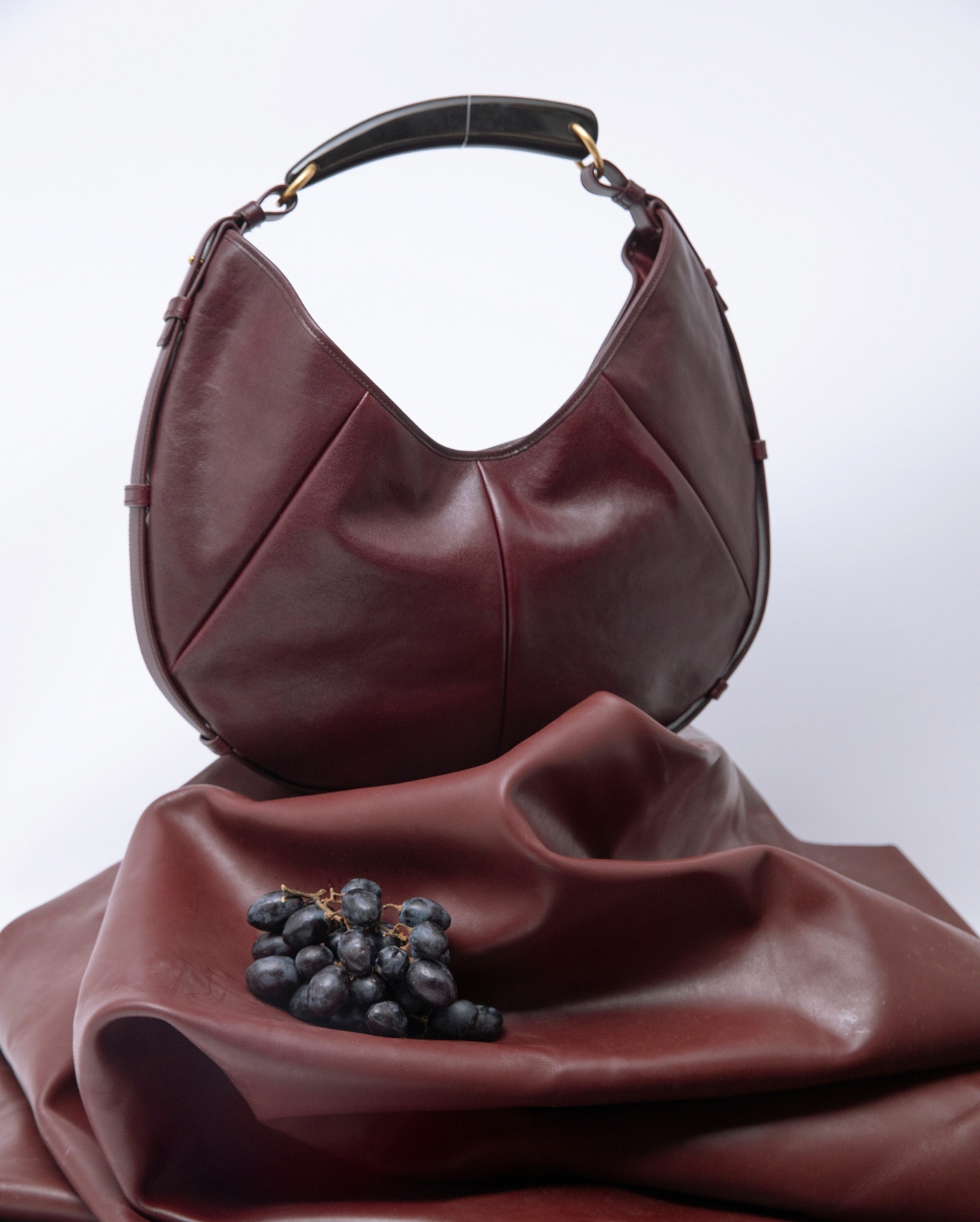 A burgundy leather bag and grapes photographed in a still life photo