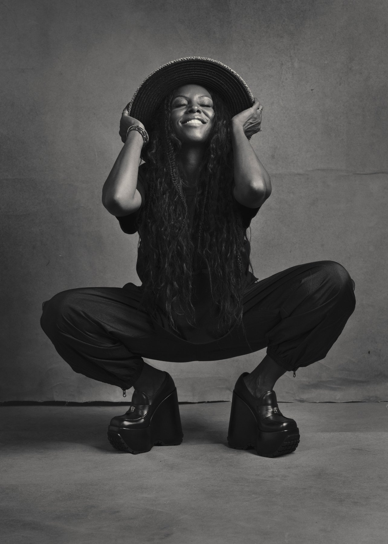 A black and white portrait of June Ambrose in a studio smiling with a hat on