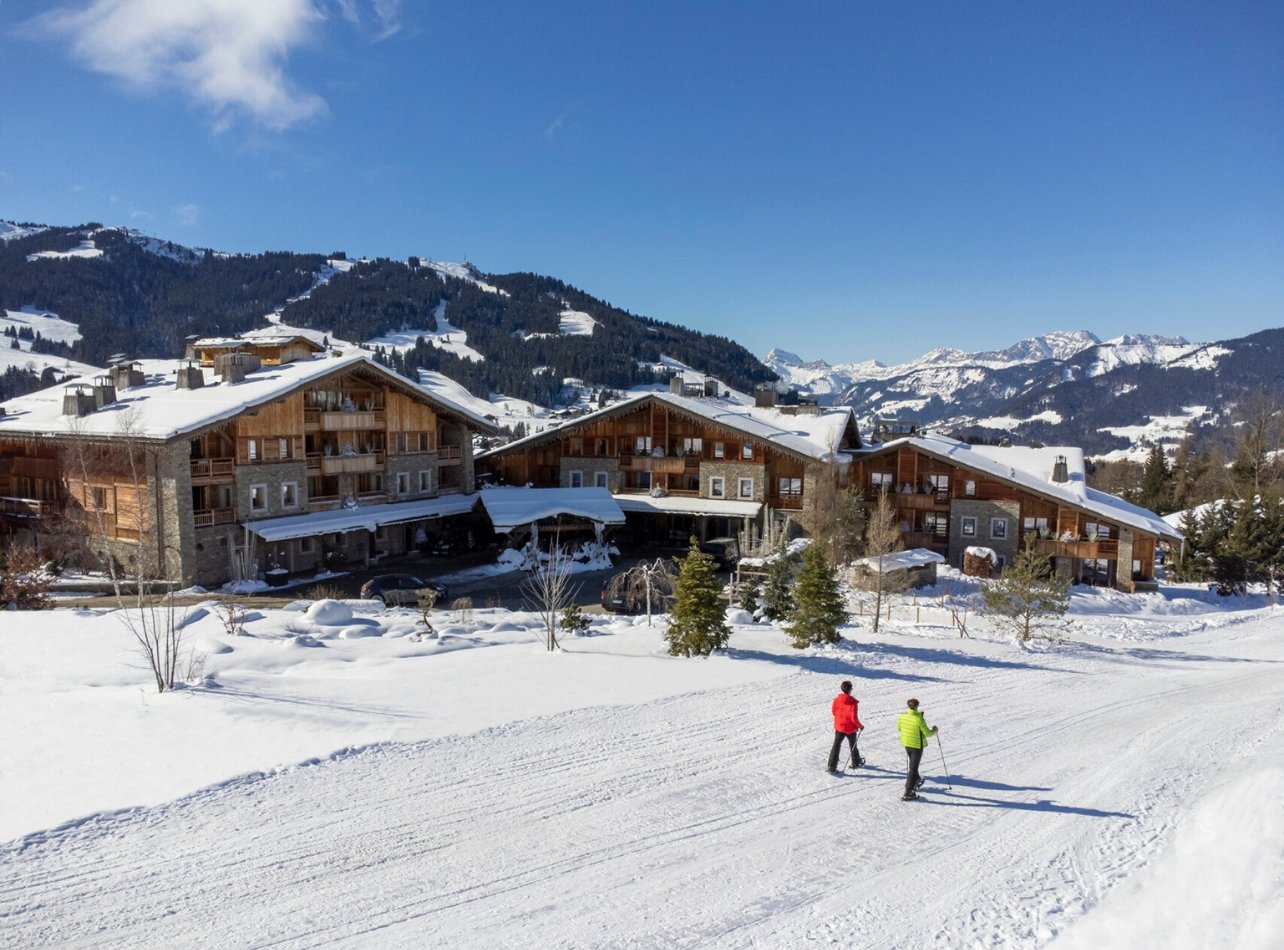 Snow path with two people skiing with wooden cabins in the back