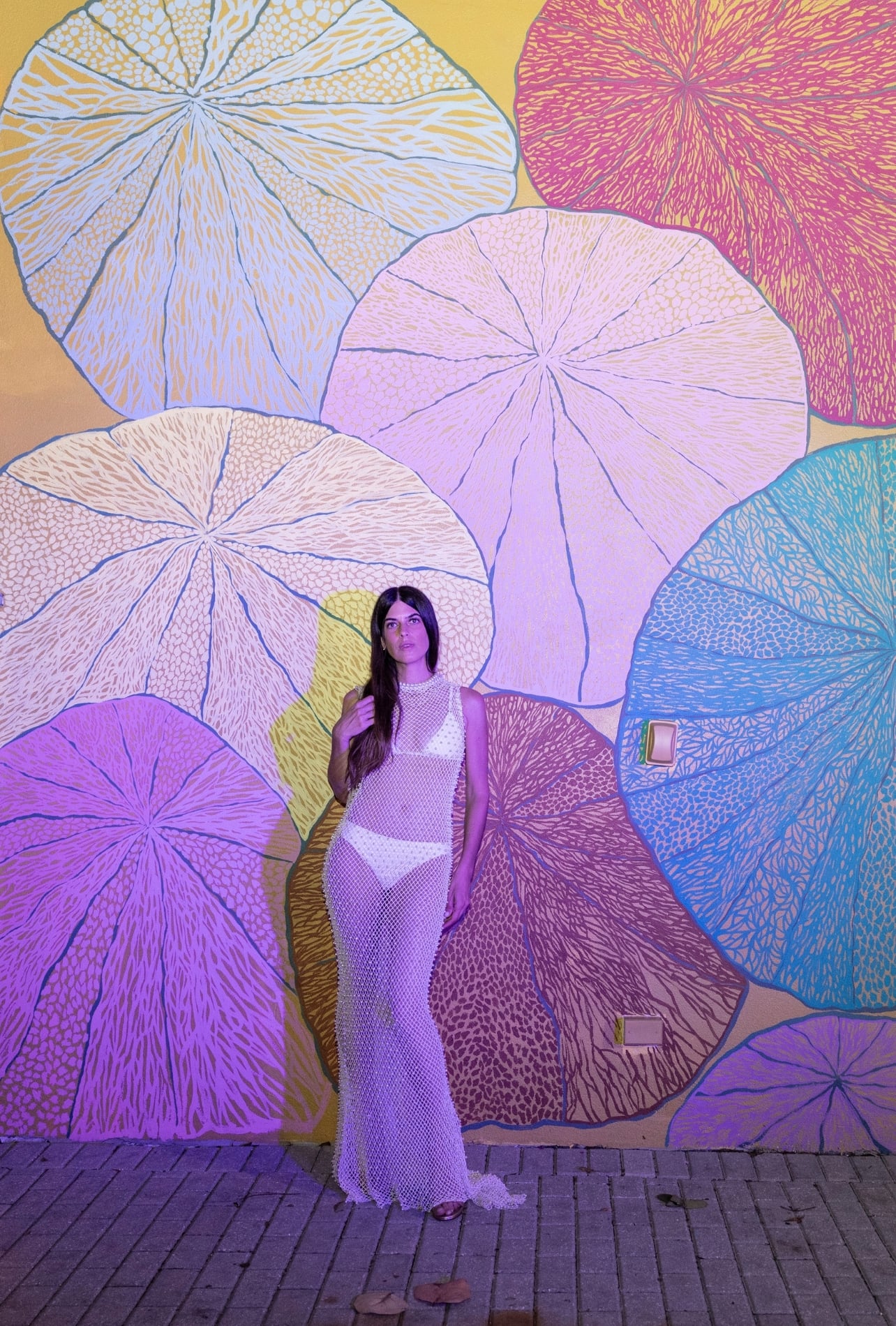 Ana Bonamico with a long white dress standing in front of a colorful painted mural