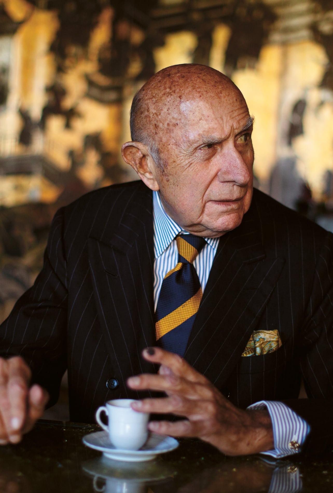 A man wearing a suit at a café with a cup of coffee
