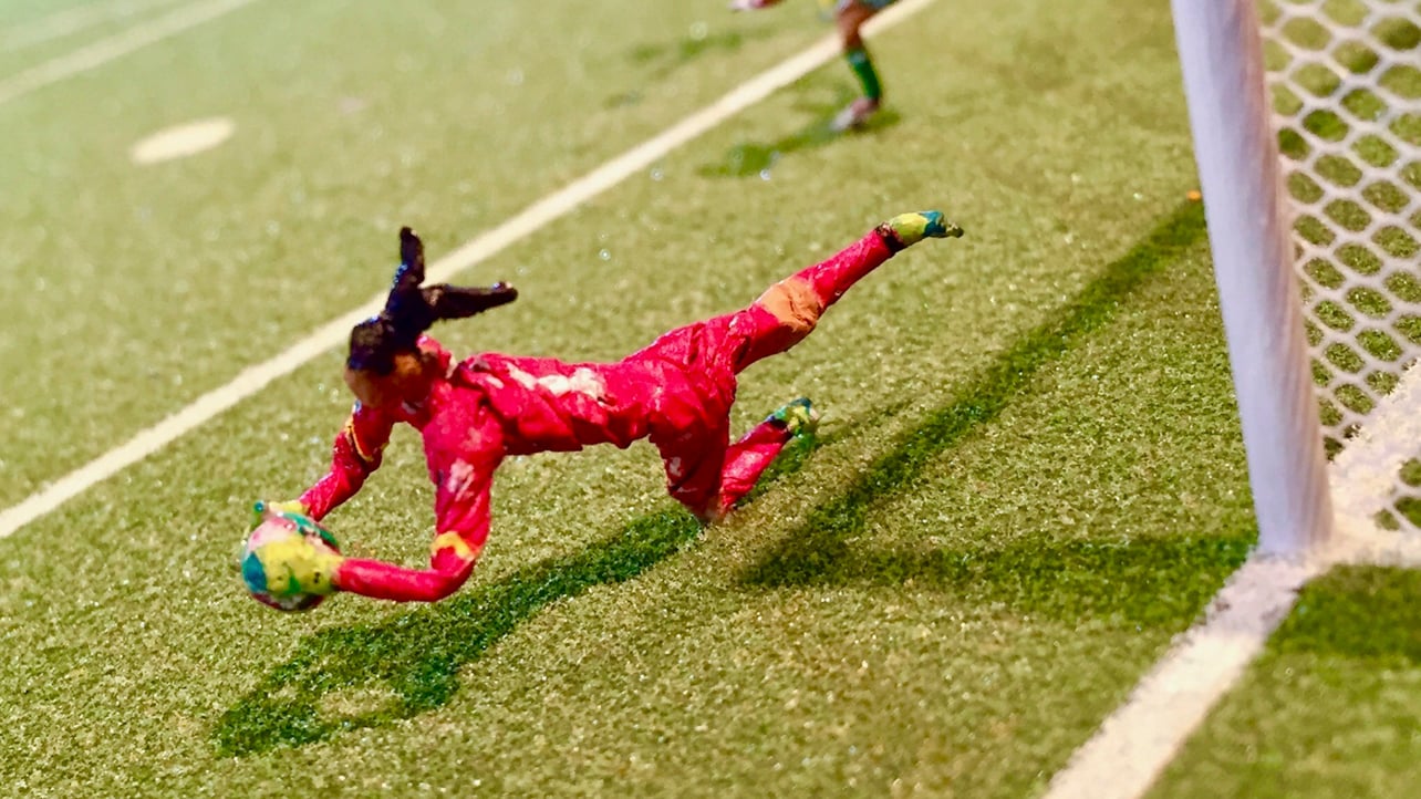 A sculpture a soccer player in a red jersey diving for the ball