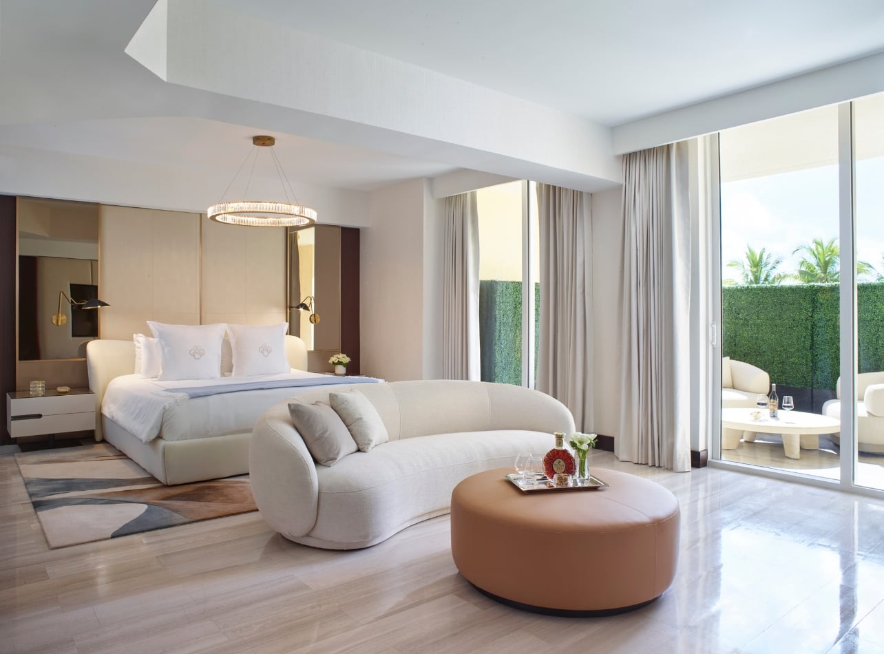 An interior of a bedroom with a couch, ottoman, and balcony