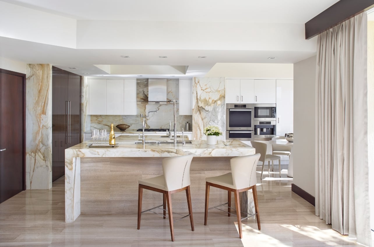 A kitchen with marble walls and counters and dark wood accents