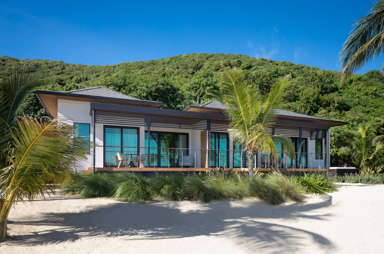 An exterior of a villa surrounded by palm trees and sand