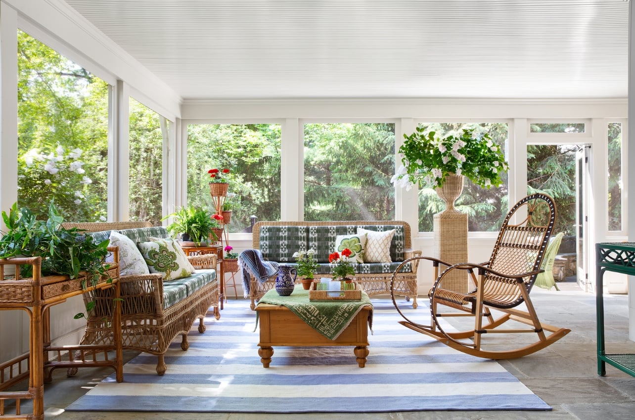 A sunroom filled with plants and rattan furniture from the book, The Happy Home