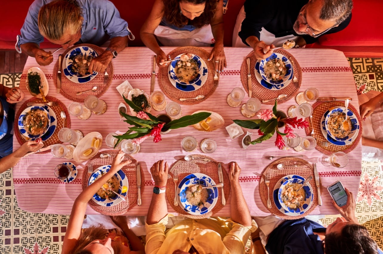 A large dinner table setting with a group of people from the book, Revel