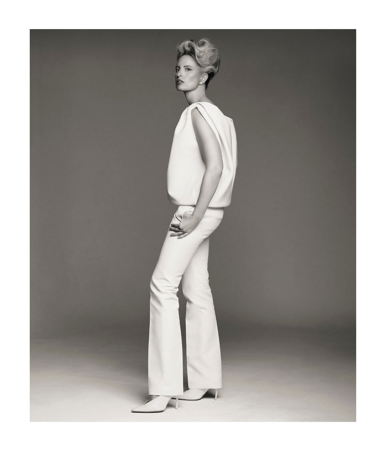 A woman wearing a white top with flared white pants and white heels