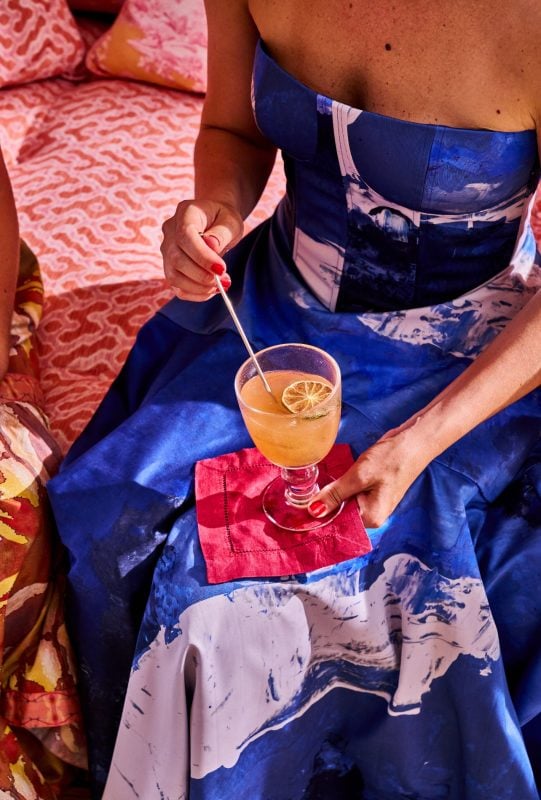 A woman wearing a blue dress holding a cocktail from the book, Revel