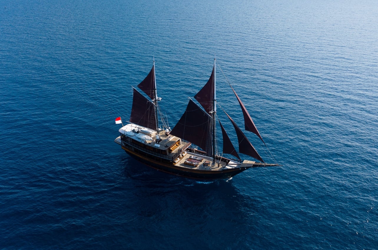 A close up aerial shot of a yacht sailing in deep blue waters