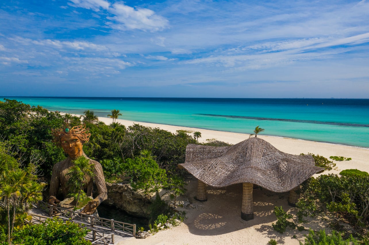An overhead shot of the beach and water with a 50-foot sculpture of the goddess made of wood