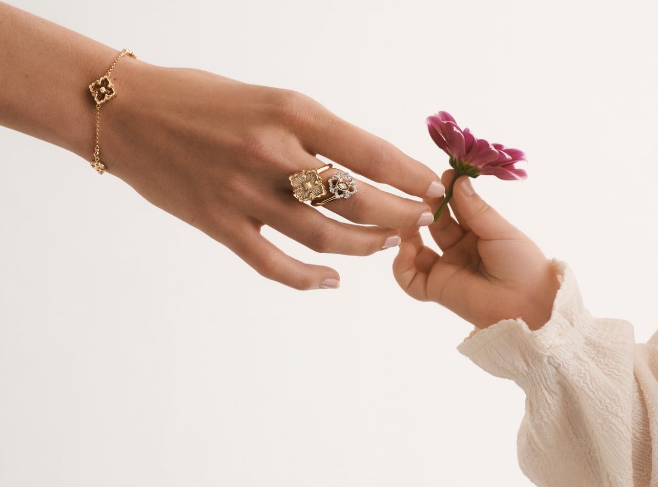 Women's hand wearing Buccellati jewelry passing a flower to a child's hand