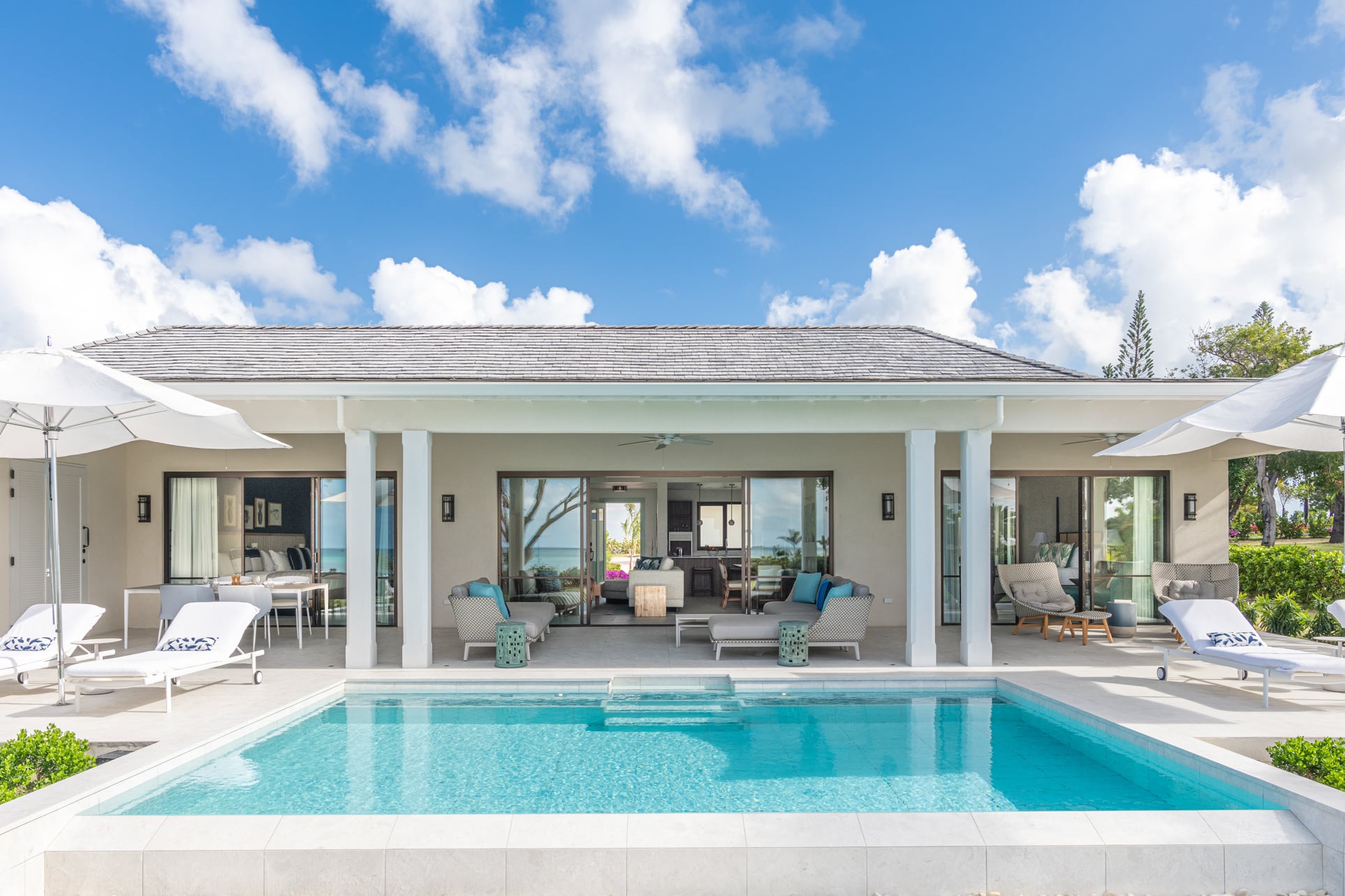 White house exterior with a pool and lounge chairs at Jumby Bay