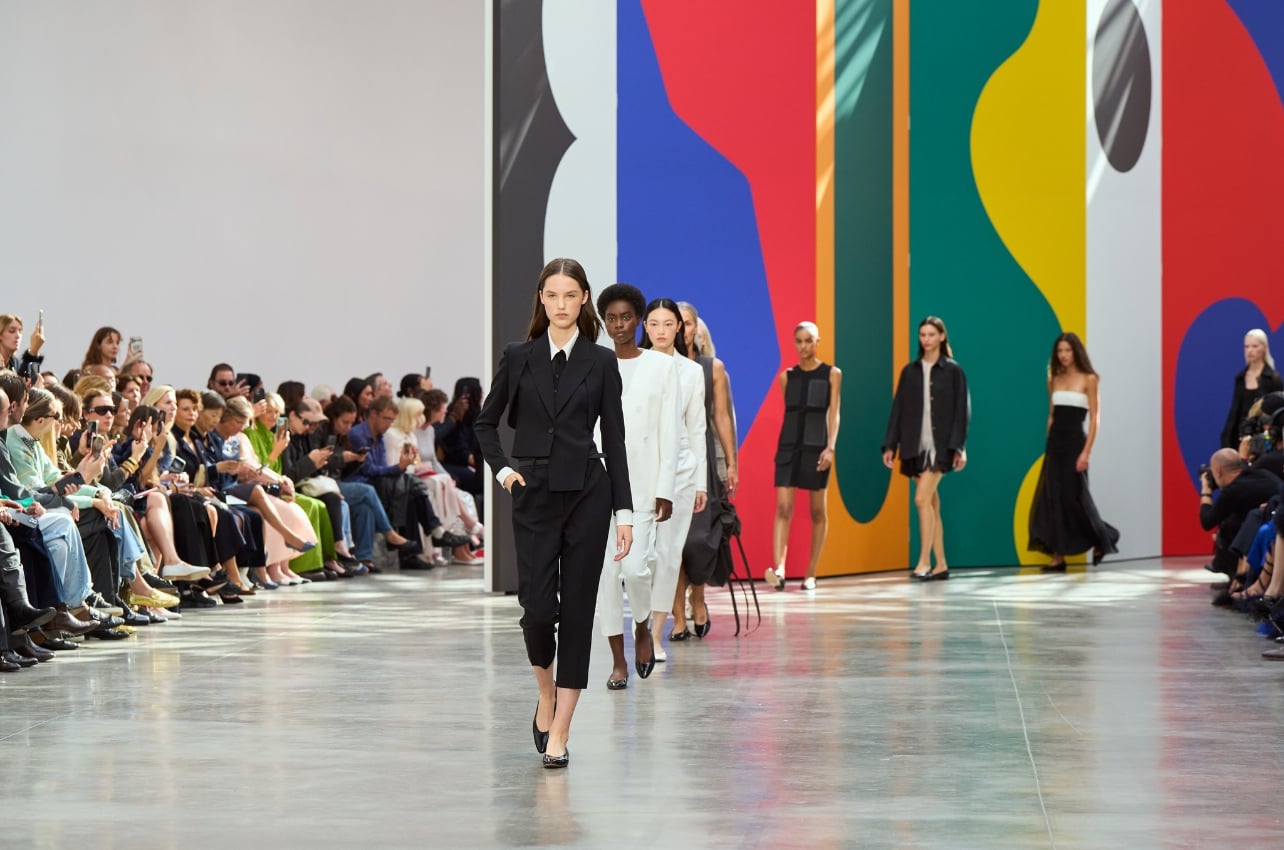 Models walking a runway in tailored black and white looks before a colorful backdrop
