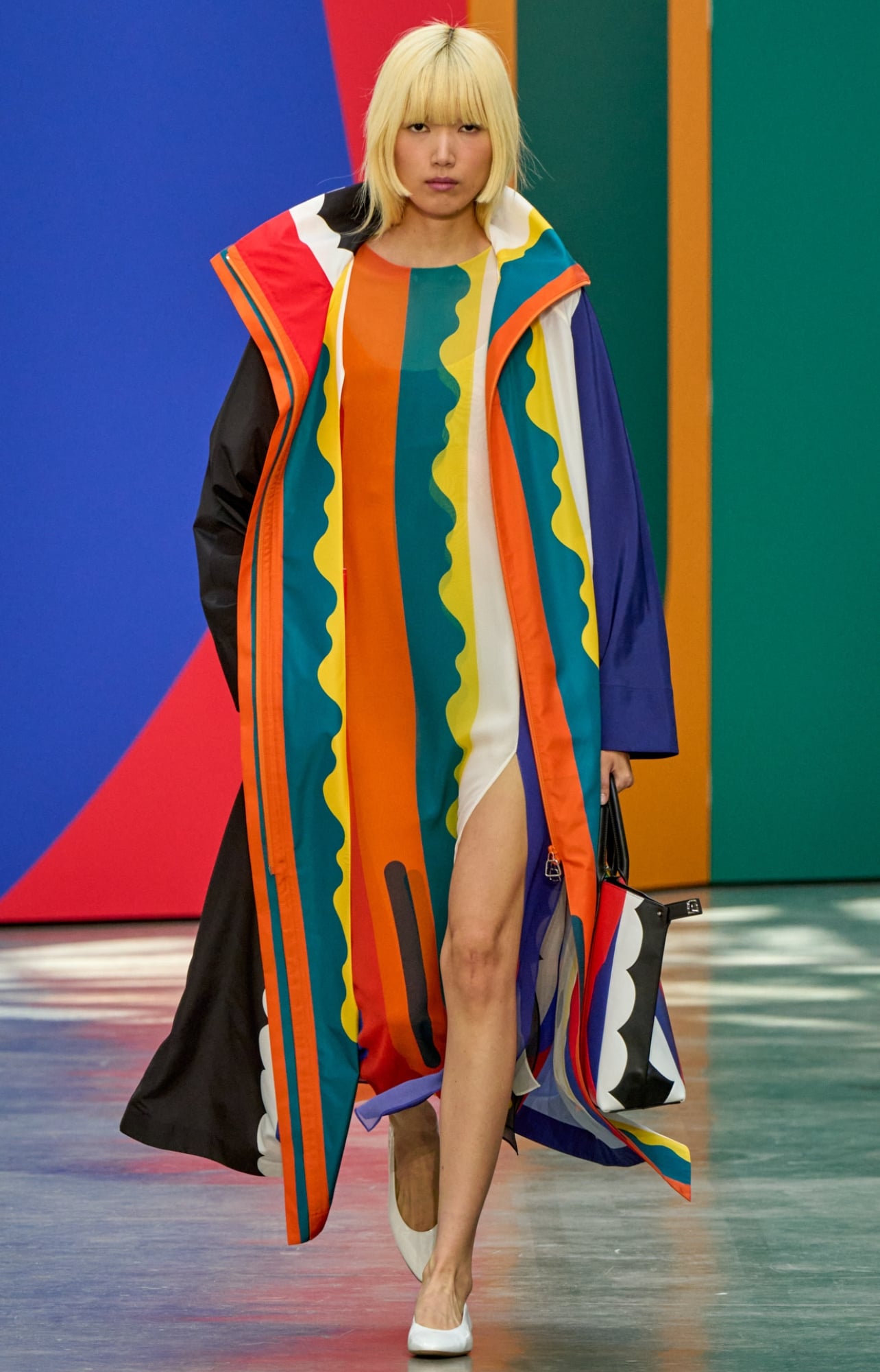 A runway model wearing a colorful dress and white heels