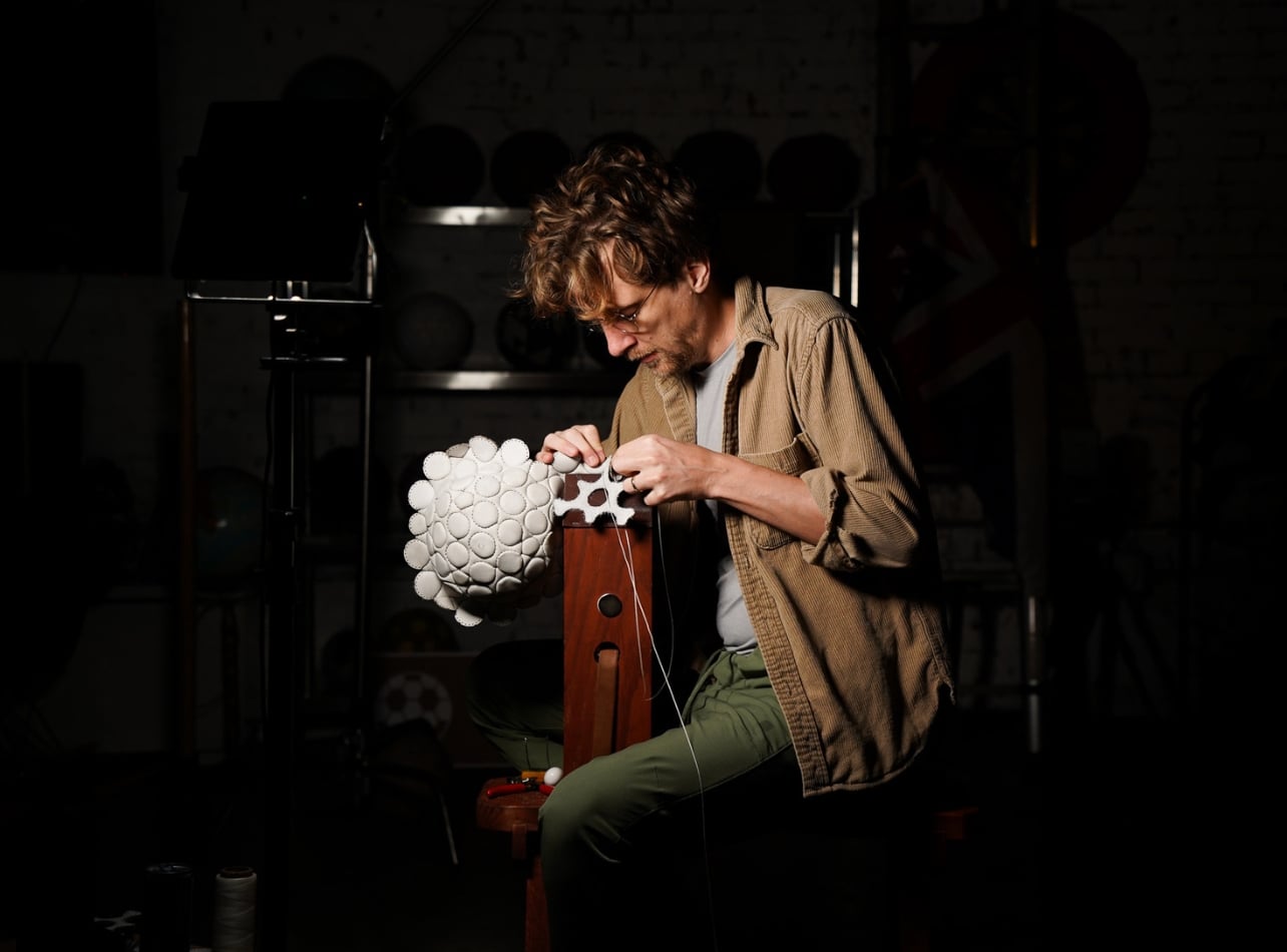 Jon Paul Wheatley-sitting in a black room sewing a white ball