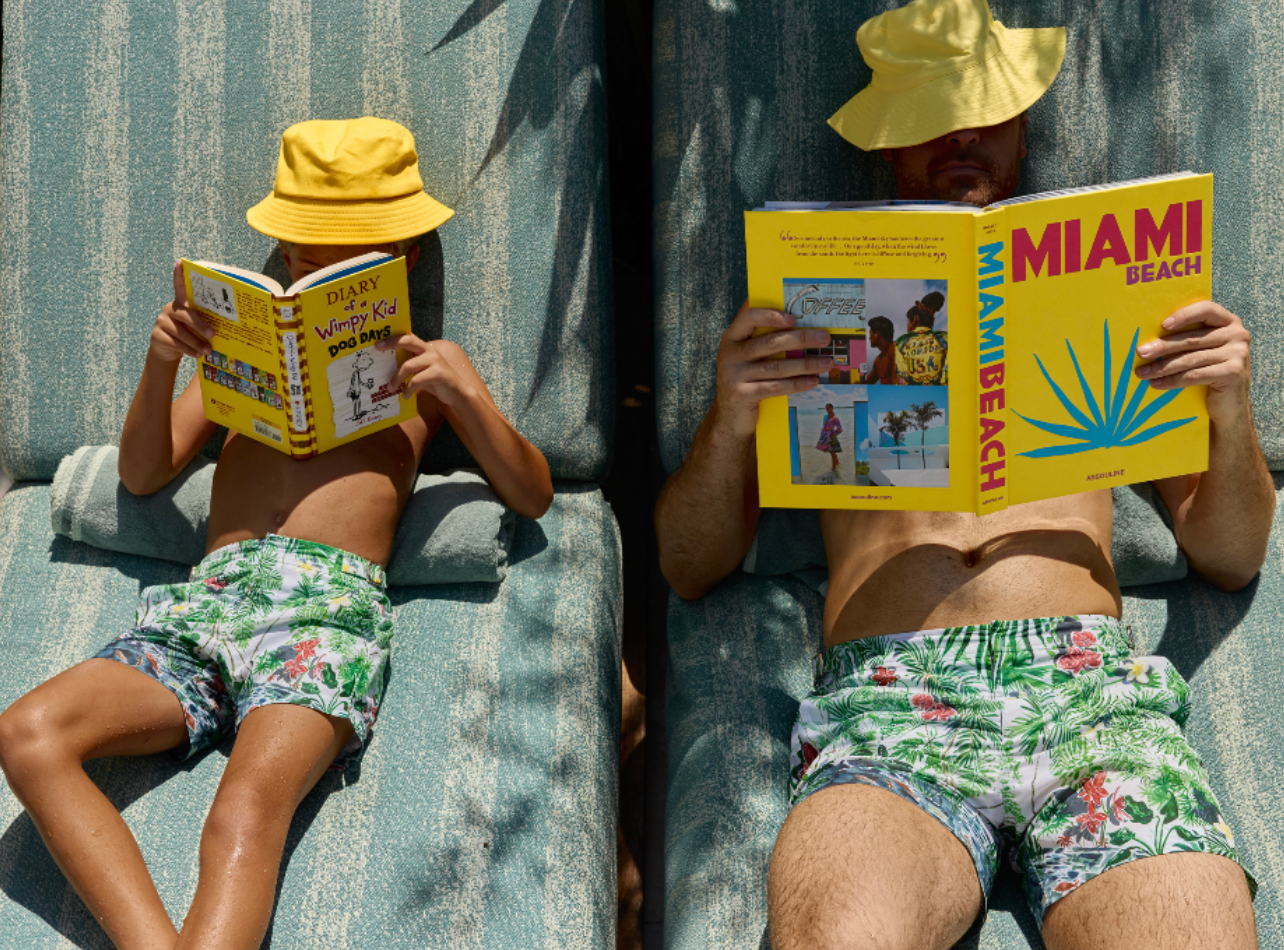 A father and son reading books on beach chairs