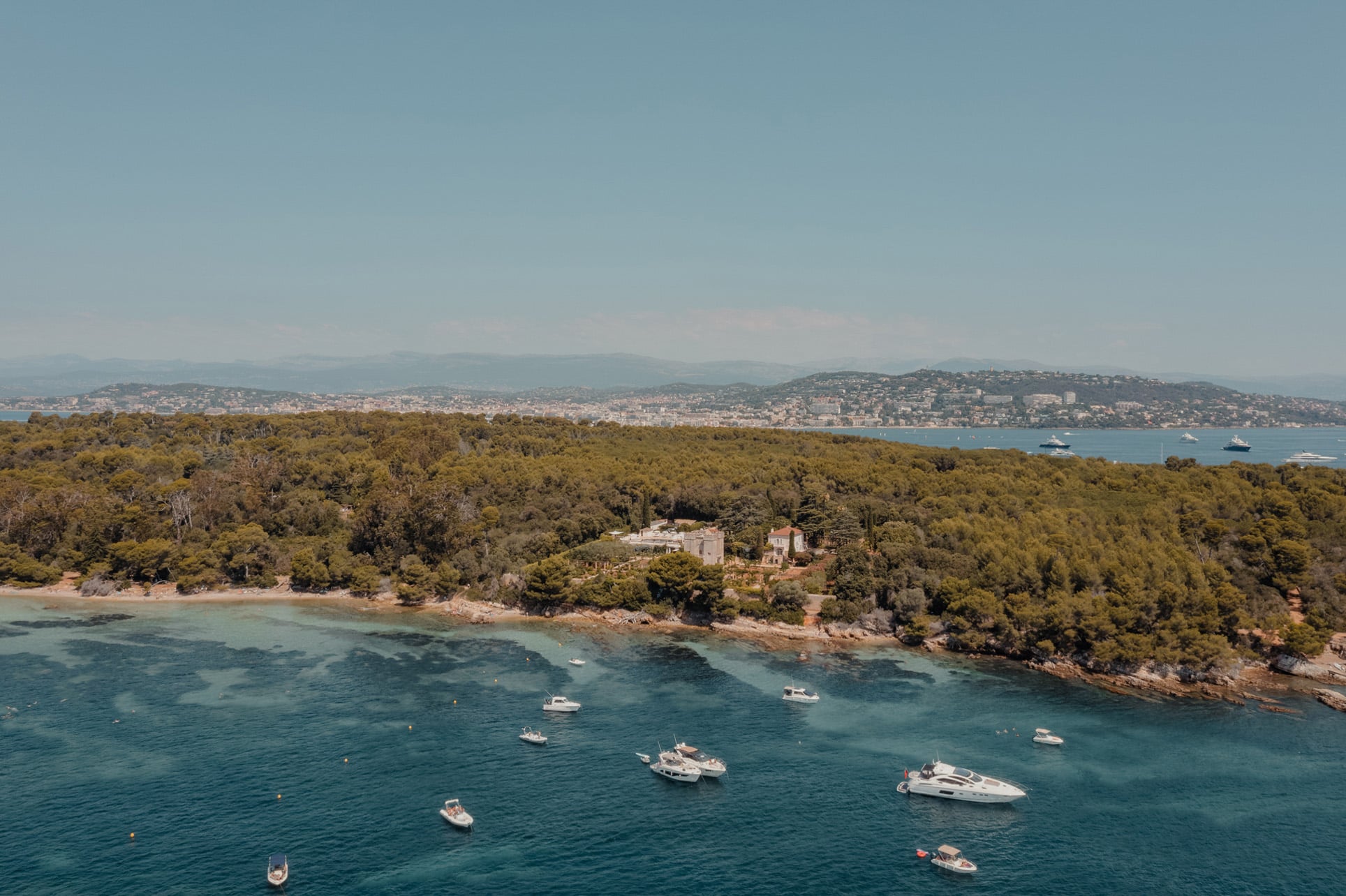 An aerial landscape view of boats on the water beside a luxury villa property surrounded by lush greenery