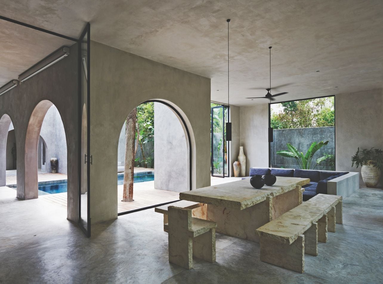 A pool deck with a seating area featuring a stone dining table and couch
