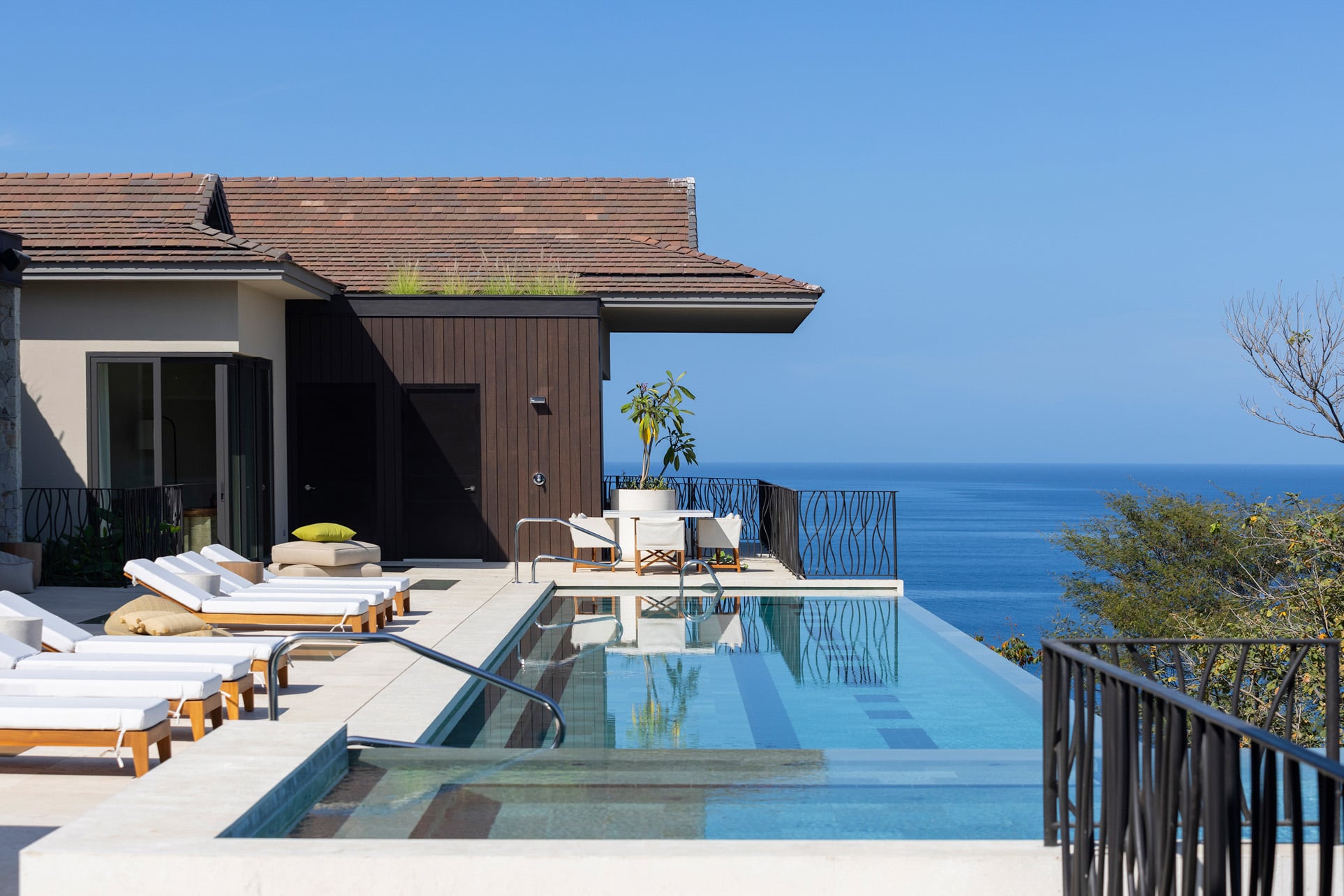 An infinity pool beneath blue skies on a villa rooftop overlooking the surrounding landscape