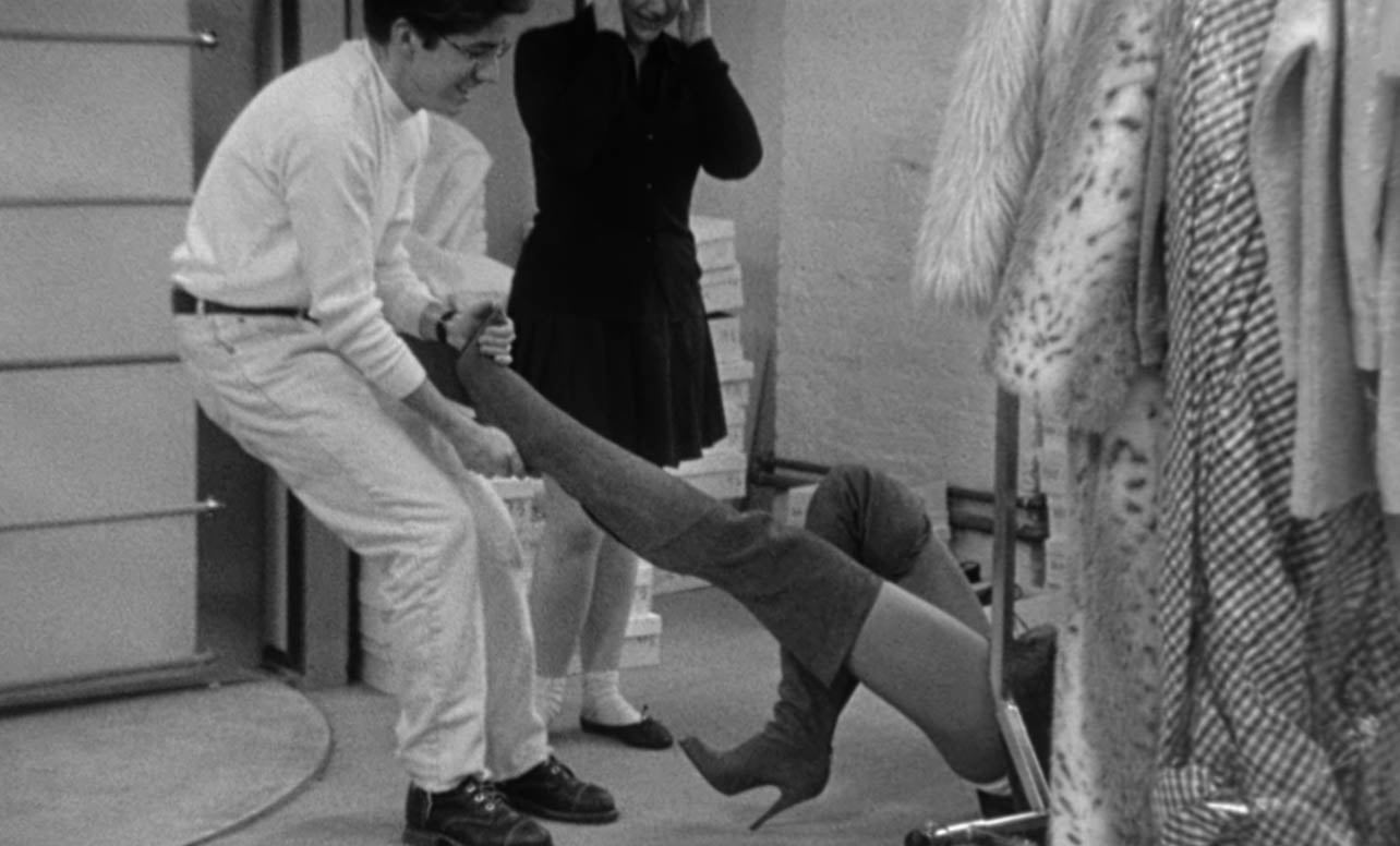 A black and white archival photo of a model taking her tall boots off