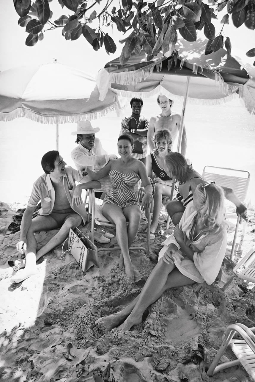 A black and white vintage photograph of a group of people sitting on a beach