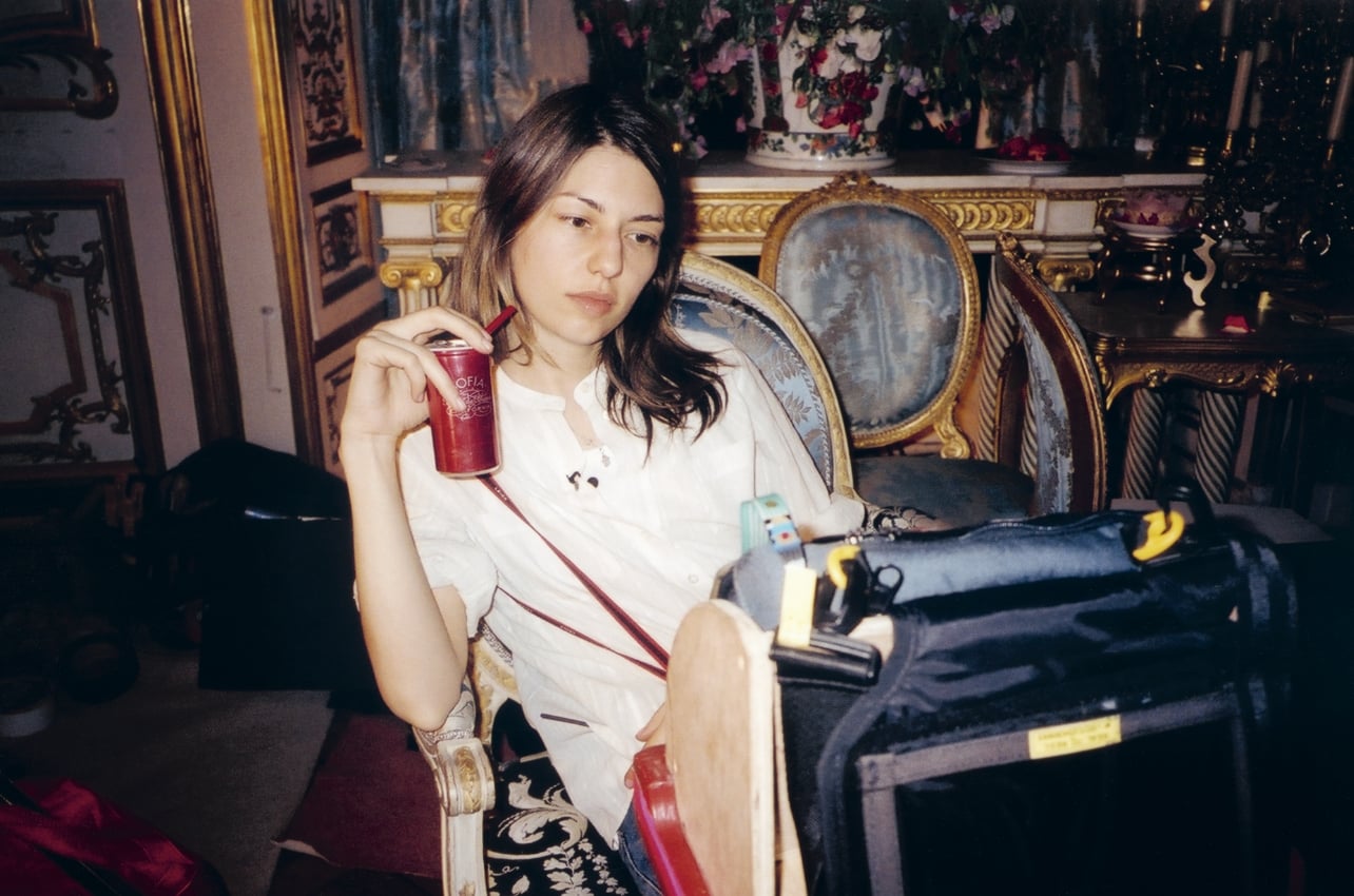 A photograph of a woman sitting in a chair with a drink in her hand