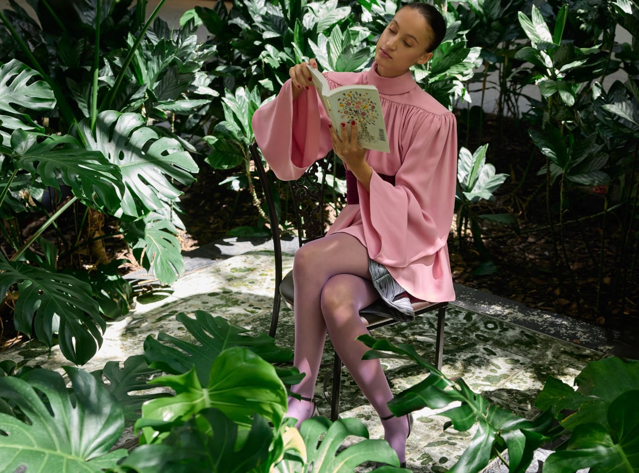 A model wearing a pink dress in a garden with a book